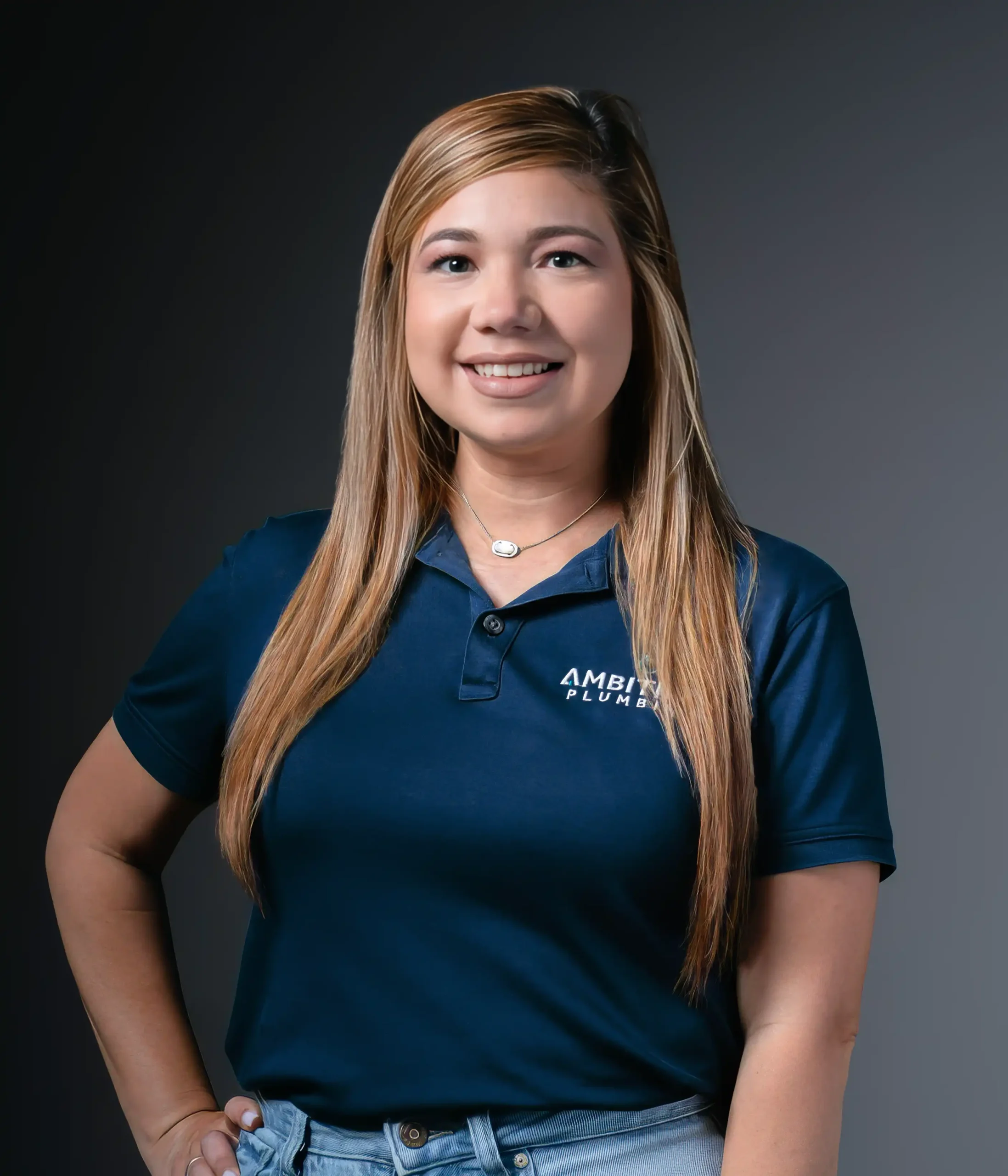 About Ambitious Plumbing co-owner Chelsey Castro wearing a branded navy polo shirt in a professional staff portrait