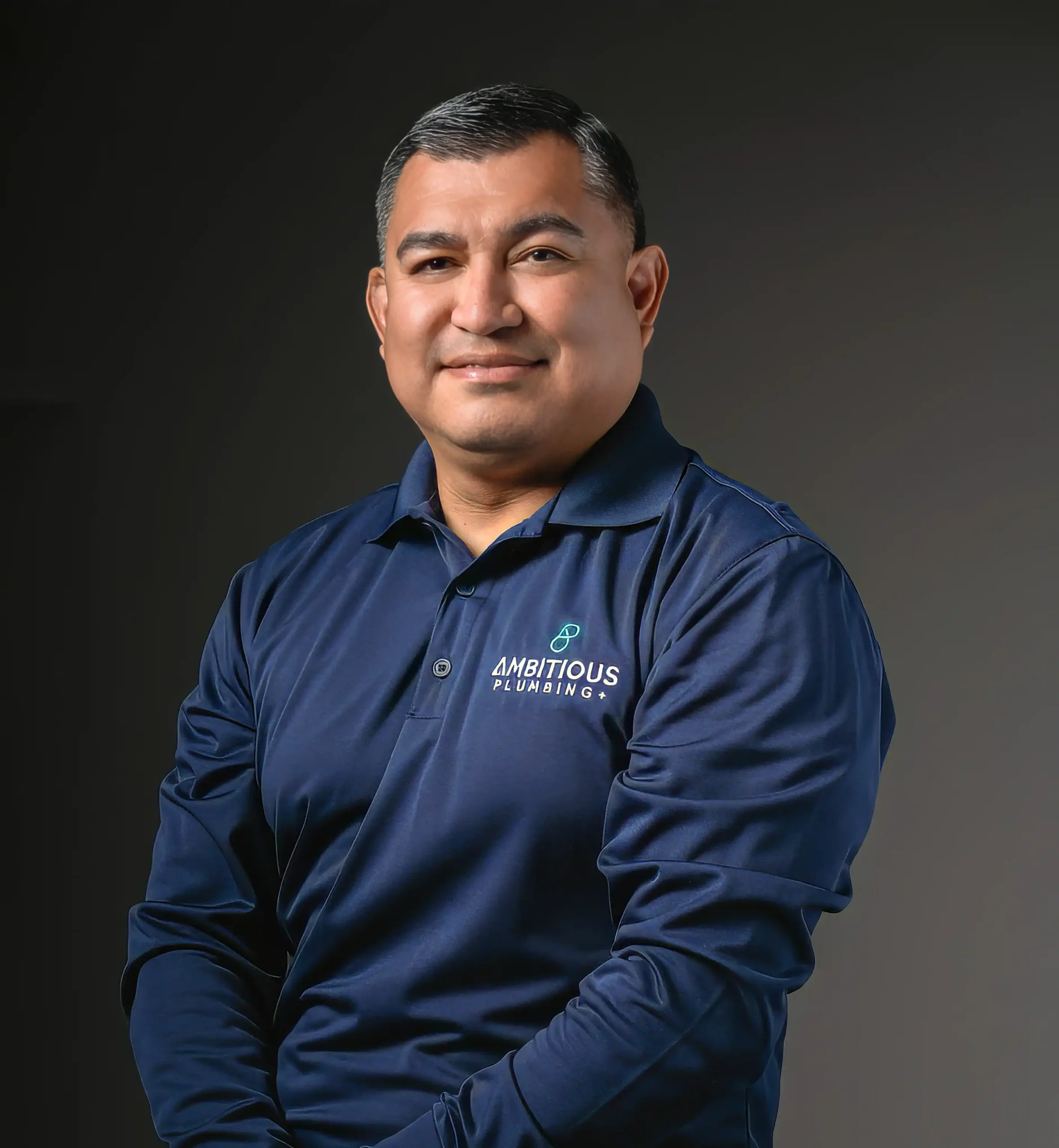 About Ambitious Plumbing founder Chris Castro wearing a branded navy blue polo shirt in a professional headshot