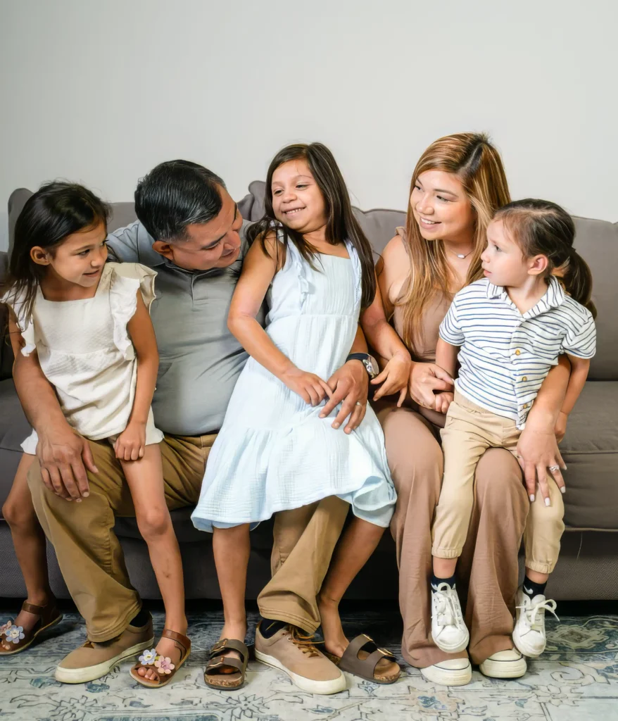Ambitious Plumbing owners Chris and Chelsey Castro smiling and talking candidly with their three children on a couch