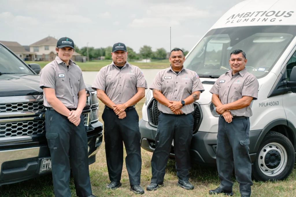 Four uniformed Ambitious Plumbing technicians standing in front of branded service truck and van in League City