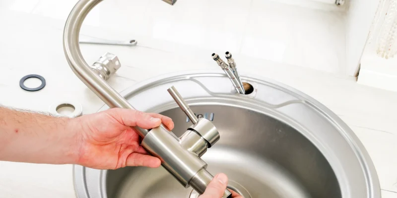 Close-up of hands installing a modern stainless steel kitchen faucet into a sink in a League City home